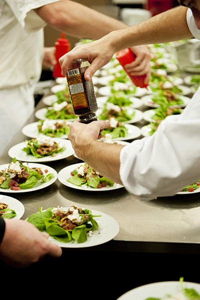 Chef and staff add dressig to rows of salads