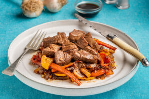 food photograph of balsamic beef with onions carrots and peppers on a white plate.