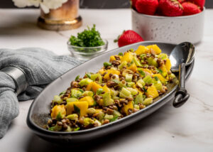 Food photograph of black lentil salad with mango and celery on a black plate.