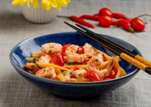 Food Photograph of Green Papaya Salad with tomatoes and hot peppers in a blue bowl.